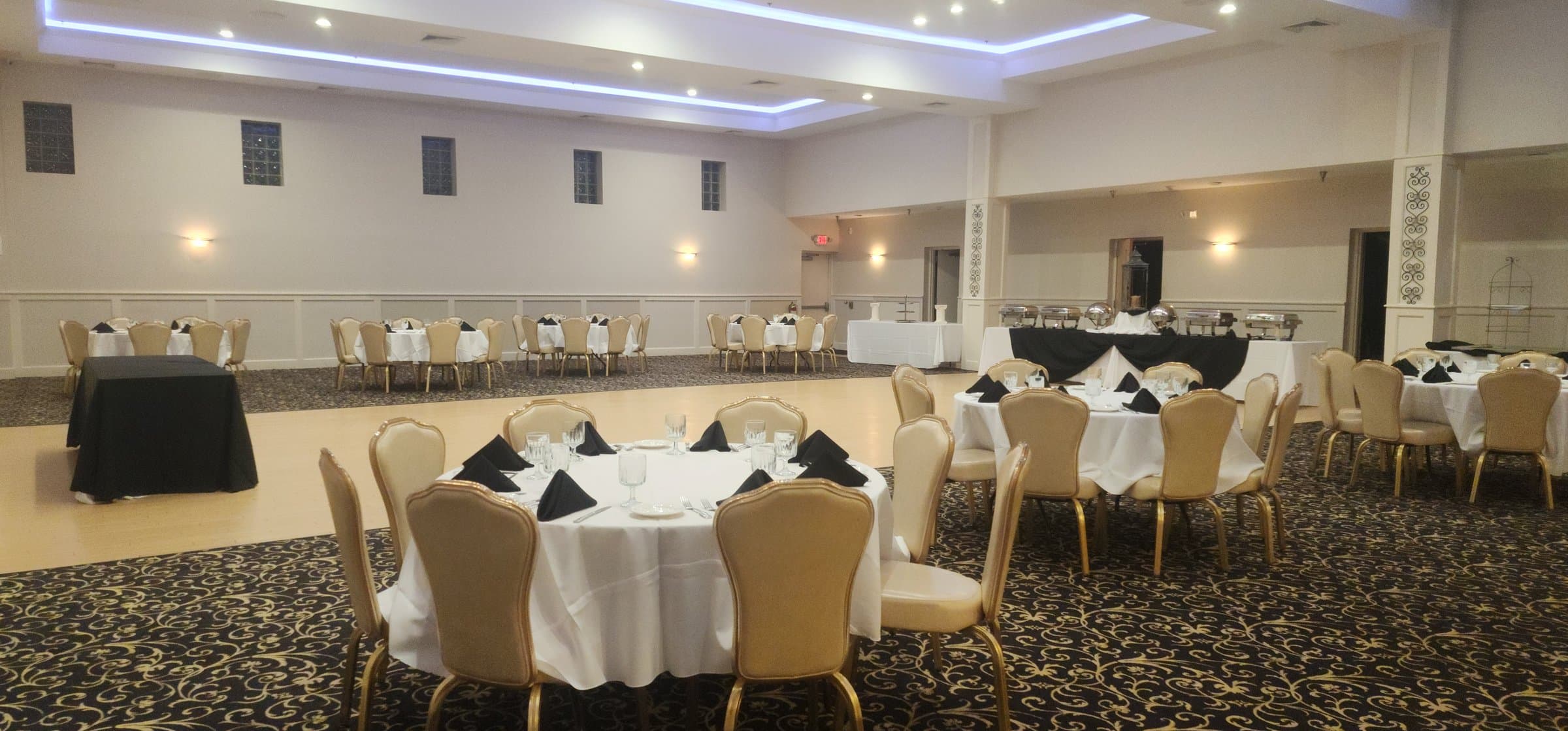 The Main Ballroom in black-and-white decor — round tables with white linen and black napkins, a draped buffet, and blue cove lighting